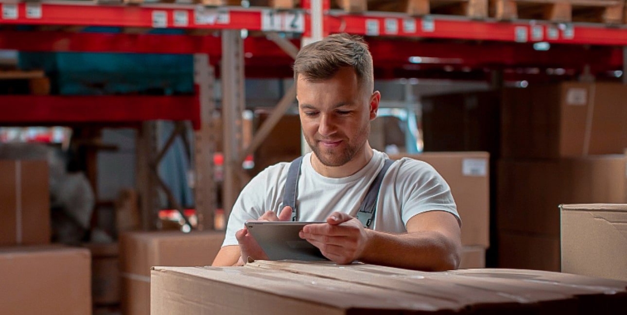 Profissional de logística fazendo anotações em um tablet no estoque cheio de uma distribuidora